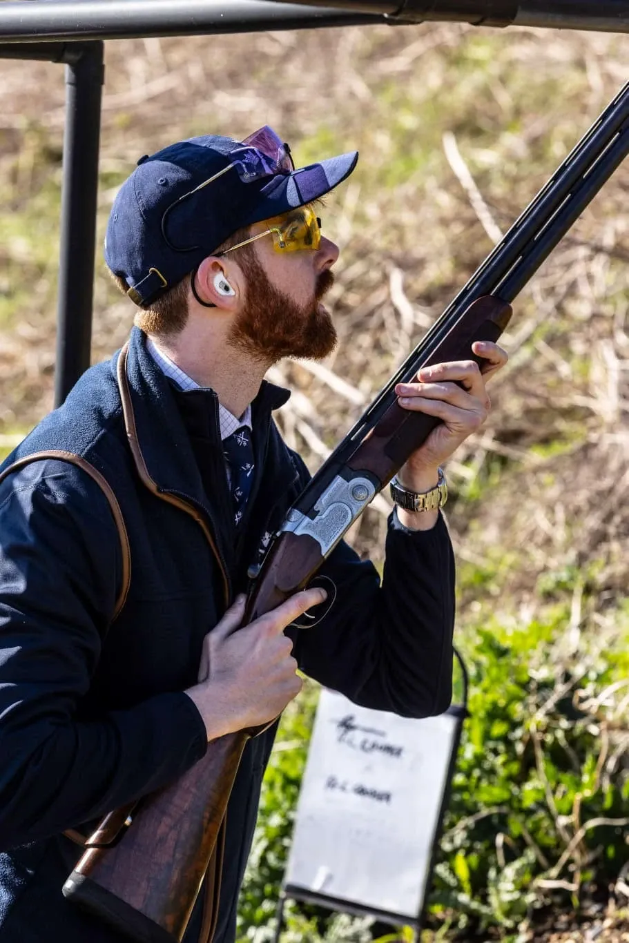 A member in club kit and shooting glasses, gun ready, watching for the clay